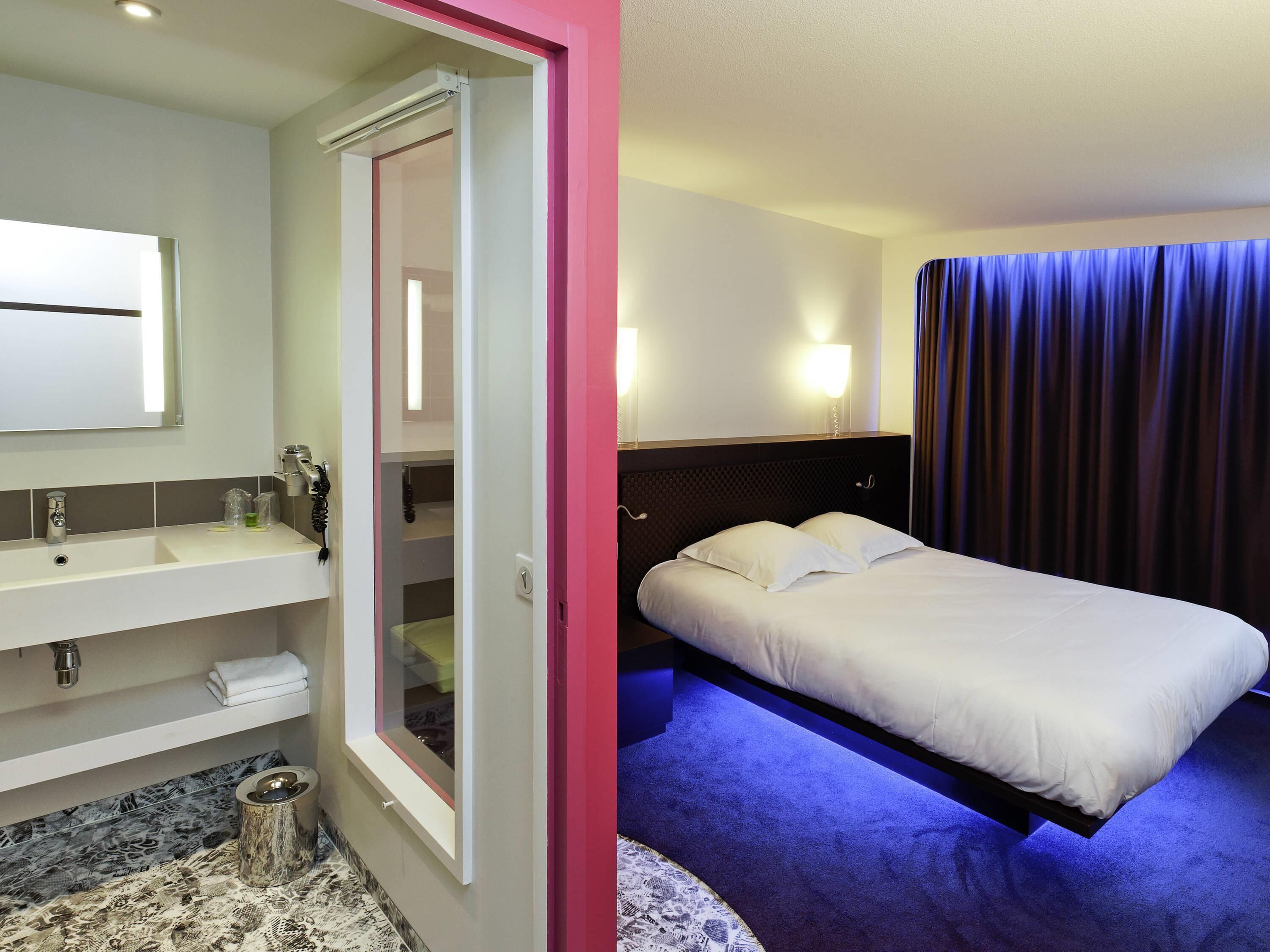 Quarto de hotel com cama, banheiro com espelho e chuveiro.