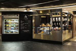 A modern café with a refrigerated display case and a counter with food items. - Pullman Paris Montparnasse Hotel (Paris)