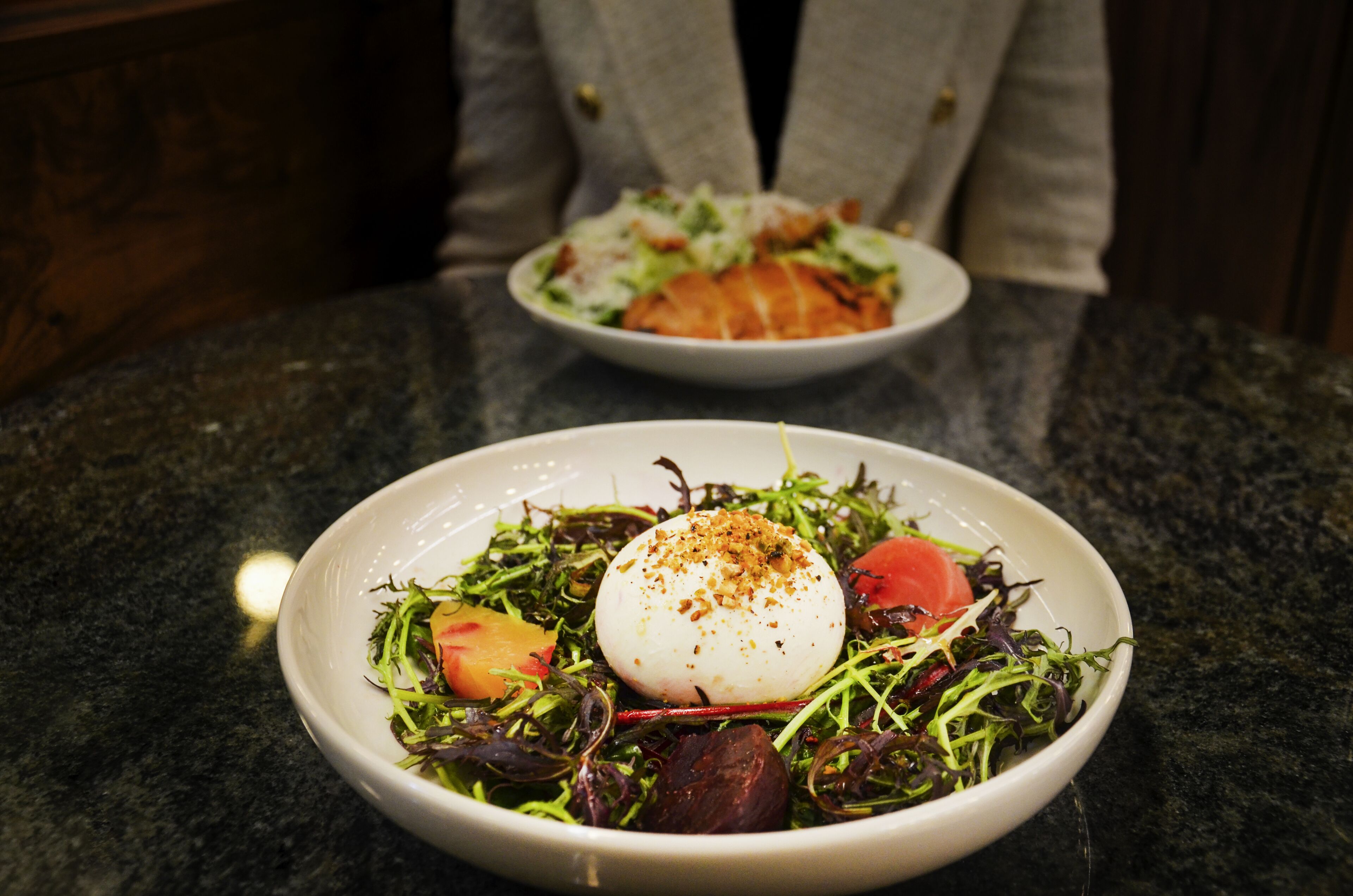 A dining table with two plates of food, one with a salad and the other with a dish that includes a poached egg.