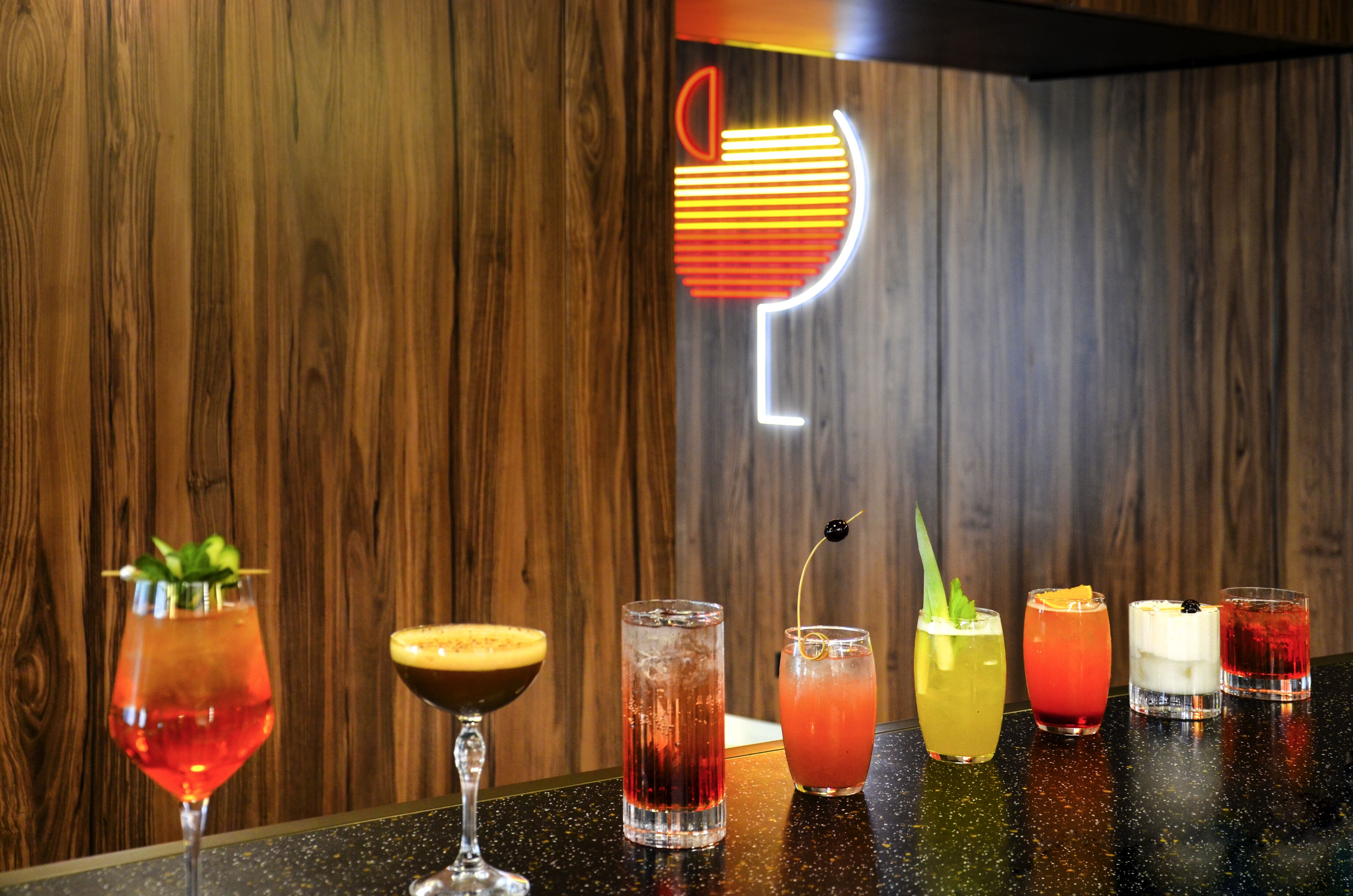 A bar area with various cocktails and a neon sign in the background.