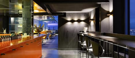 Un área de bar moderna con una barra larga, taburetes y vistas de la ciudad a través de amplios ventanales.