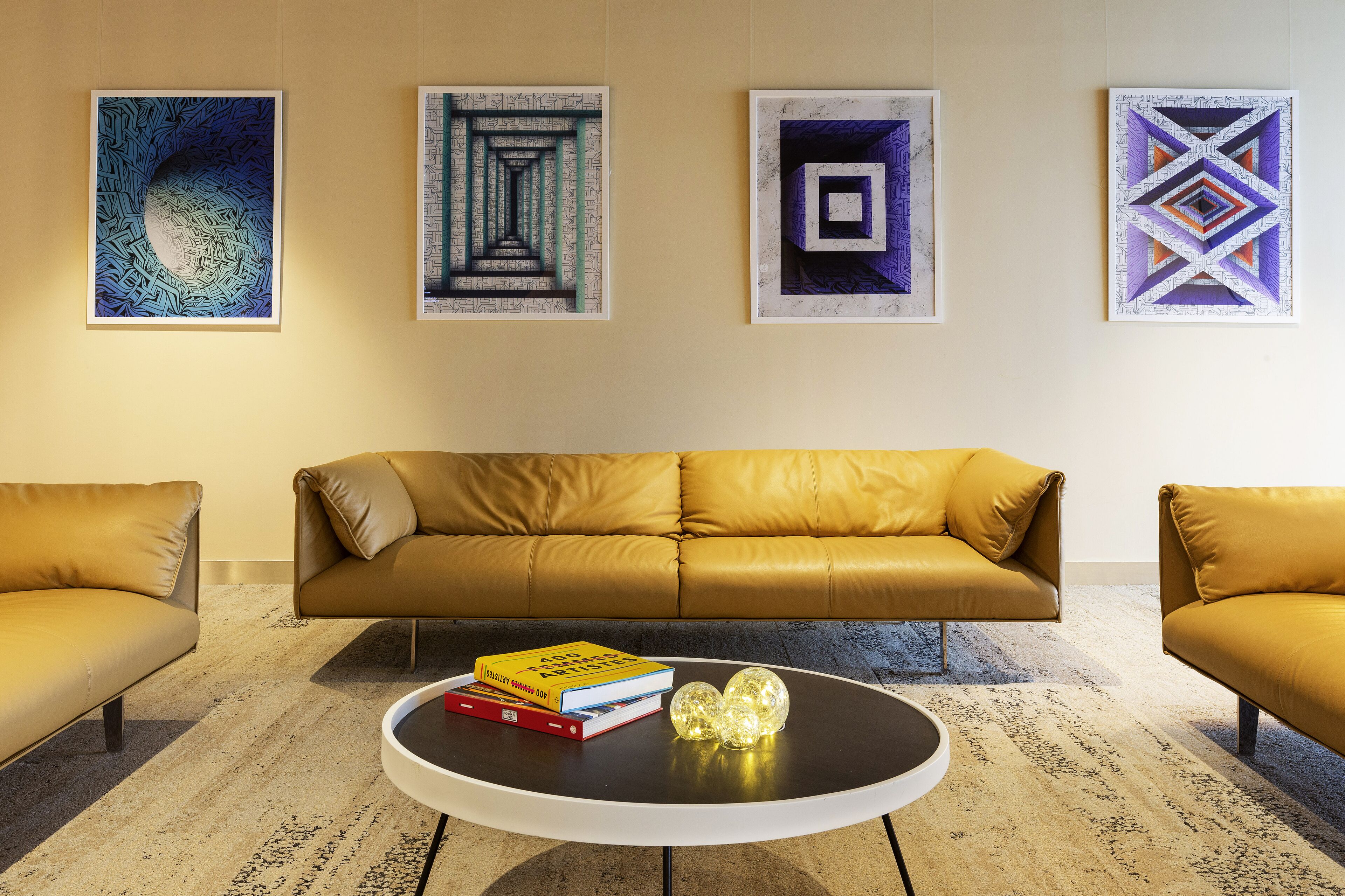 A modern living room with a brown leather sofa, a coffee table with books and decorative items, and abstract art on the wall.