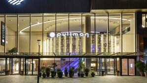 A modern hotel entrance with a glass facade, potted plants, and an illuminated sign. - Pullman Paris Montparnasse Hotel (Paris)