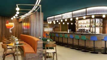 Un espace bar doté d’un comptoir incurvé, de plusieurs tabourets et d’un coin salon avec un canapé et des fauteuils.