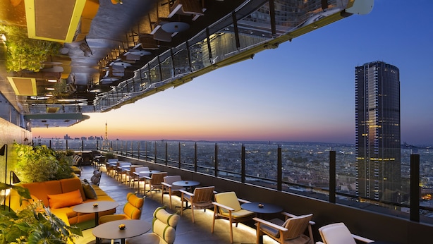 A rooftop bar with outdoor seating, a city view, and a high-rise building in the background. - Pullman Paris Montparnasse Hotel (Paris)