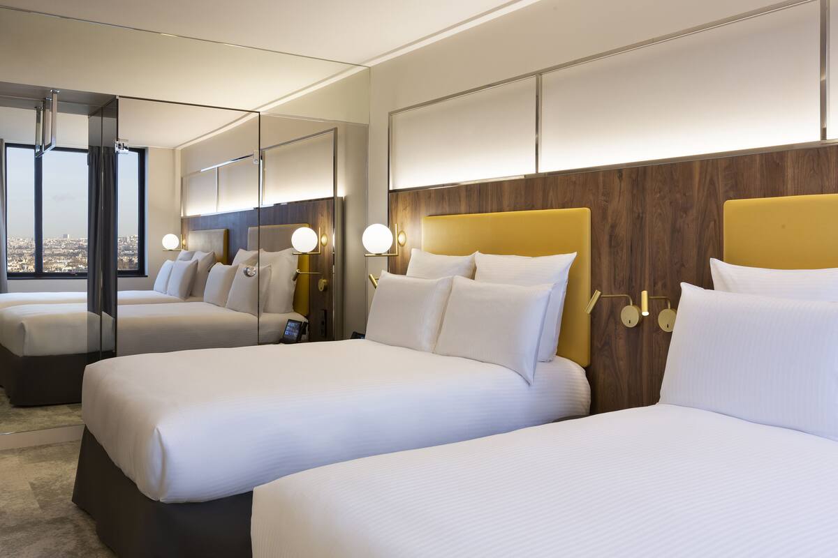 A hotel room with three beds, a large mirror, and a city view.