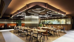 A modern restaurant with round tables and chairs, a bar area, and a large, illuminated ceiling design. - Pullman Paris Montparnasse Hotel (Paris)