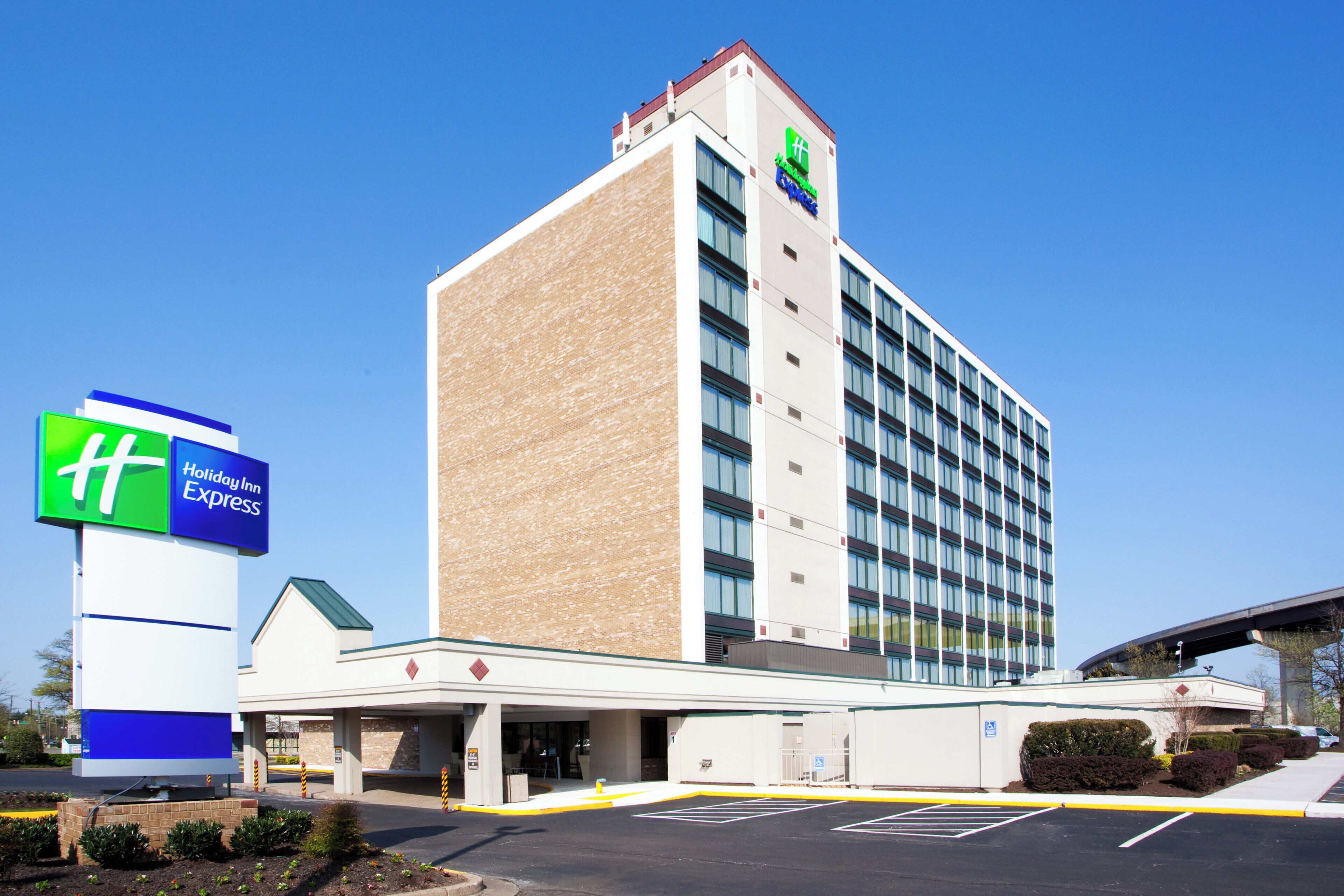 Un hotel Holiday Inn Express con diseño moderno, que cuenta con un amplio estacionamiento y un cielo despejado.