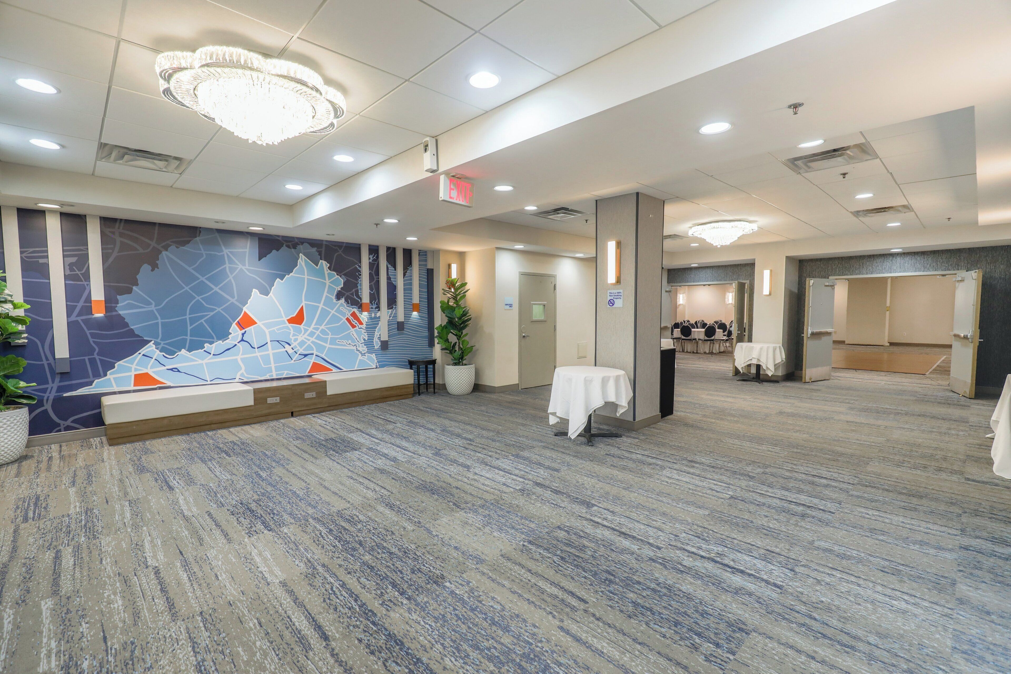 A spacious hotel lobby with a large wall mural, a reception desk, and a seating area.