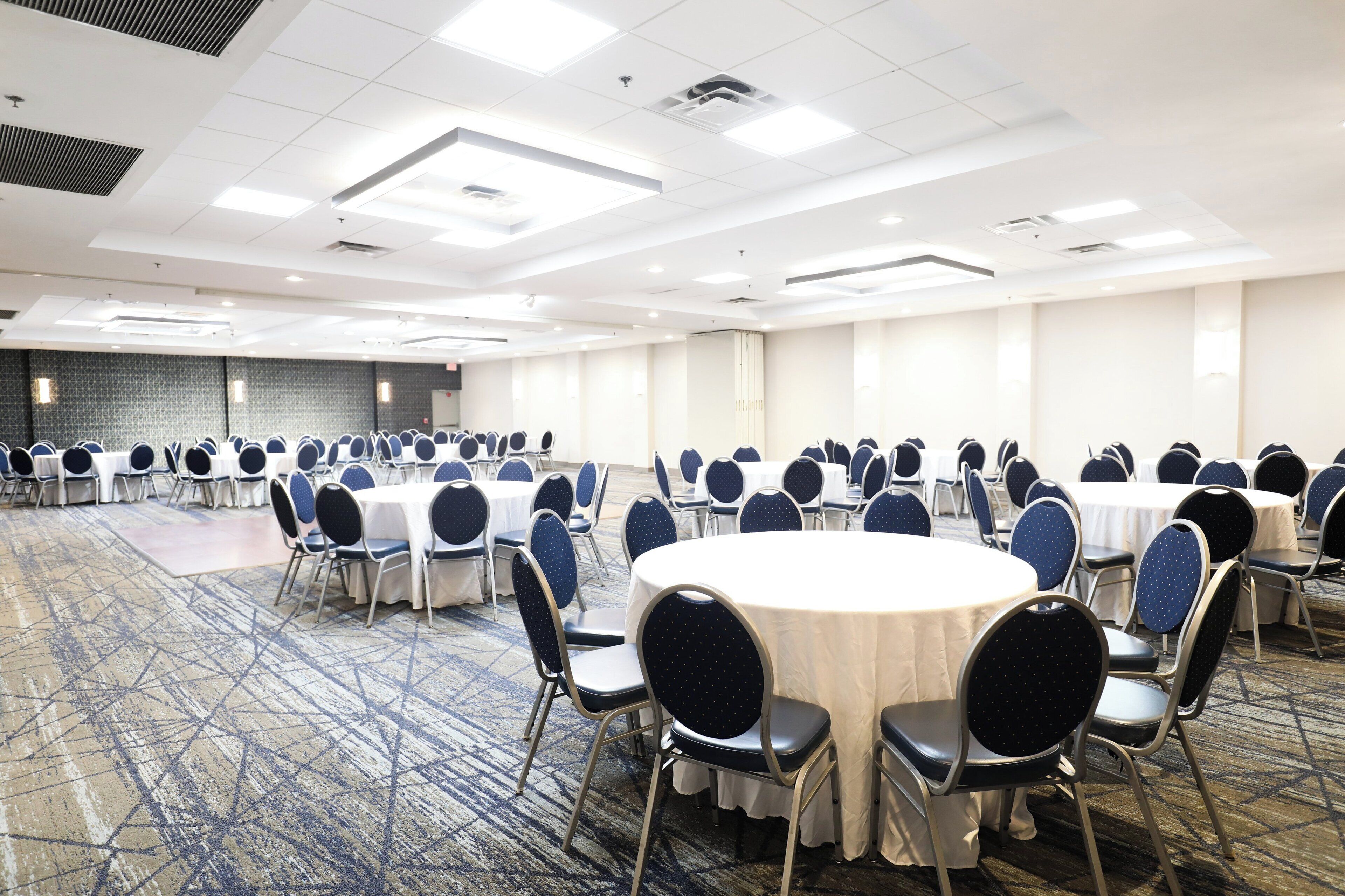 A conference room with round tables and chairs, carpeted floor, and a patterned wall.