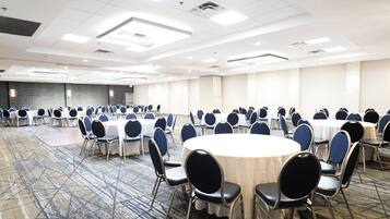 Un salón de conferencias con mesas y sillas redondas, piso alfombrado y pared con diseño.