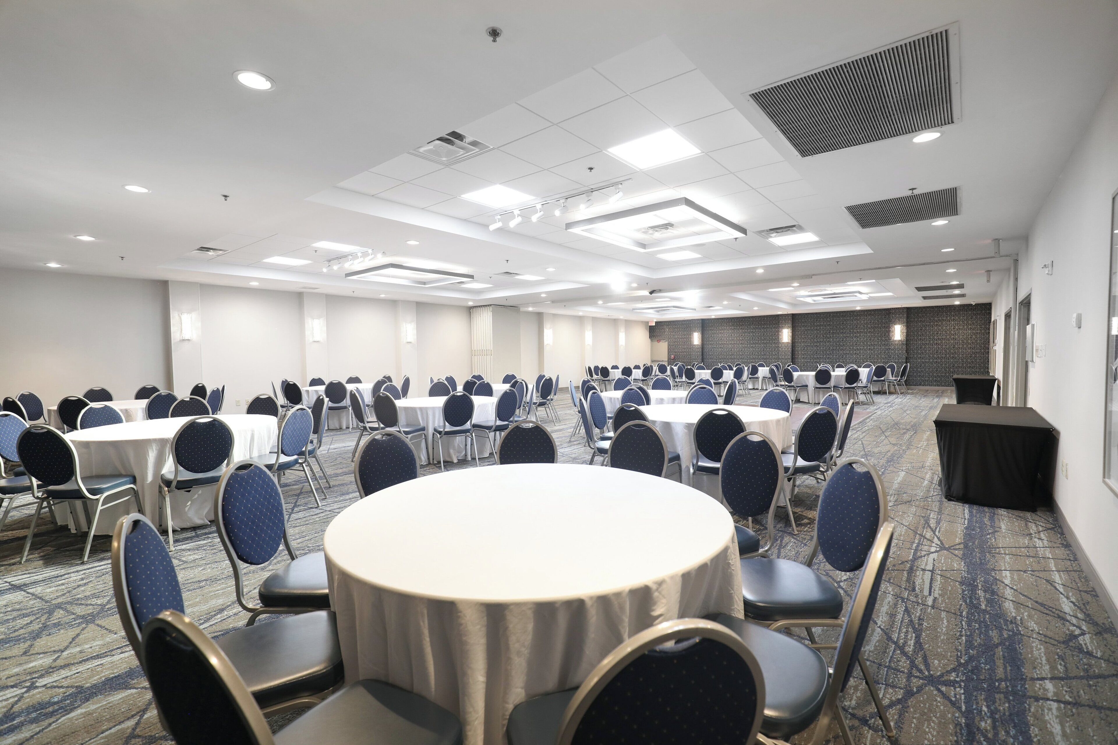 A conference room with round tables and chairs, a carpeted floor, and a high ceiling with recessed lighting.