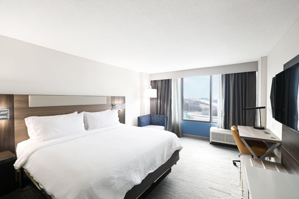 A hotel room with a large bed, a desk with a chair, a TV, and a window with curtains.