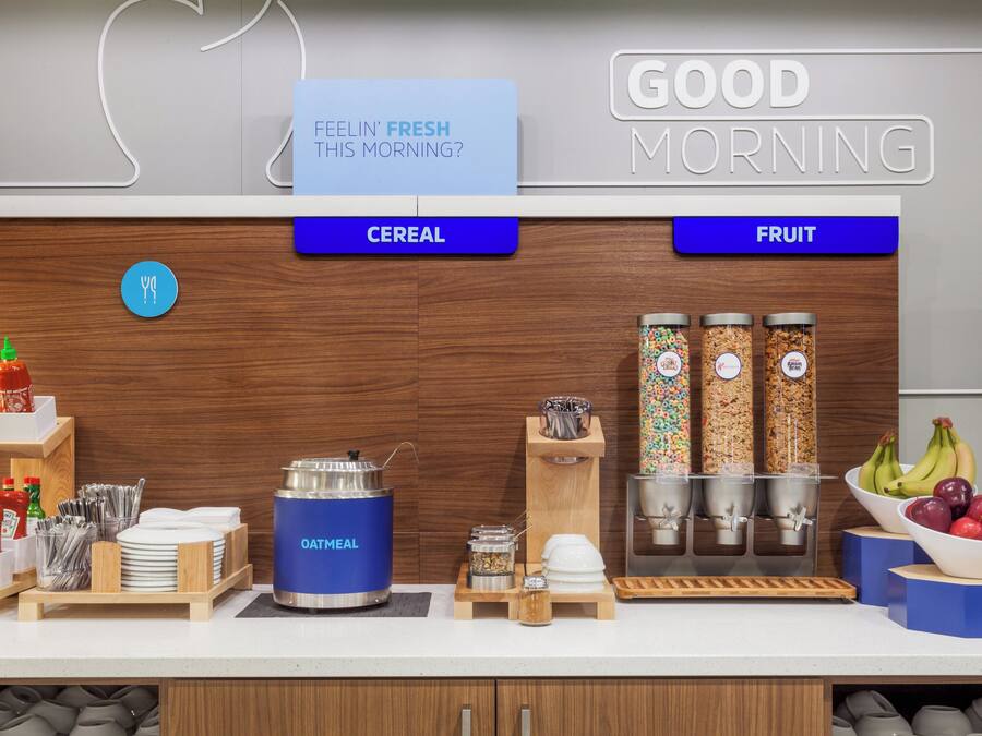 A breakfast bar with labeled sections for cereal and fruit, including a bowl of apples and bananas.