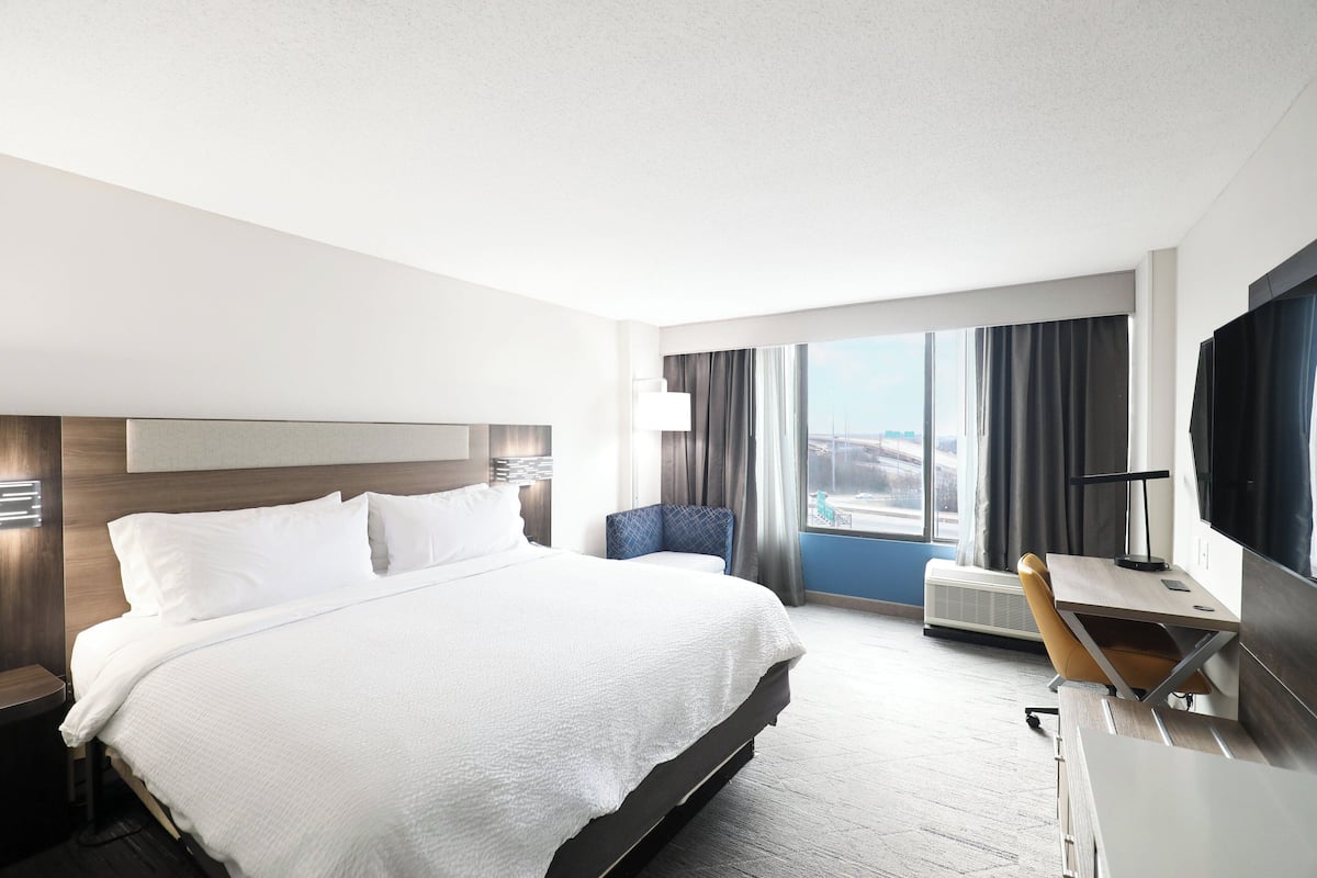 A modern hotel room with a large bed, a desk with a computer, a chair, and a TV.