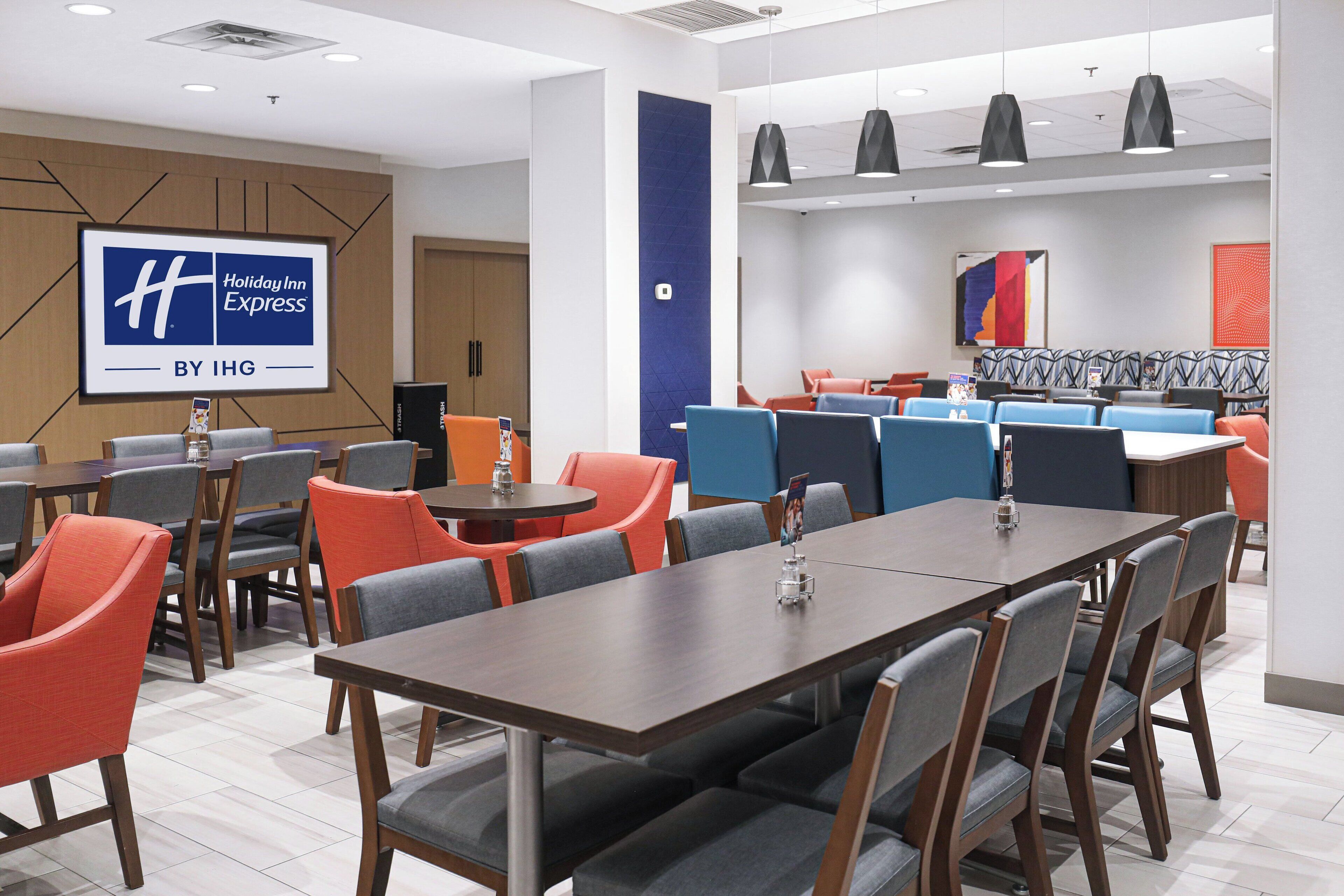A Holiday Inn Express by IHG conference room with tables, chairs, and a large screen displaying the hotel logo.
