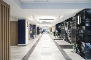 Un couloir d’hôtel moderne avec une allée centrale, des plantes en pot et des ascenseurs de part et d’autre.