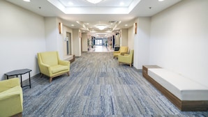 A hotel corridor with a carpeted floor, two yellow armchairs, a small table, and a bench. - Holiday Inn Express Washington DC SW - Springfield by IHG (Springfield)