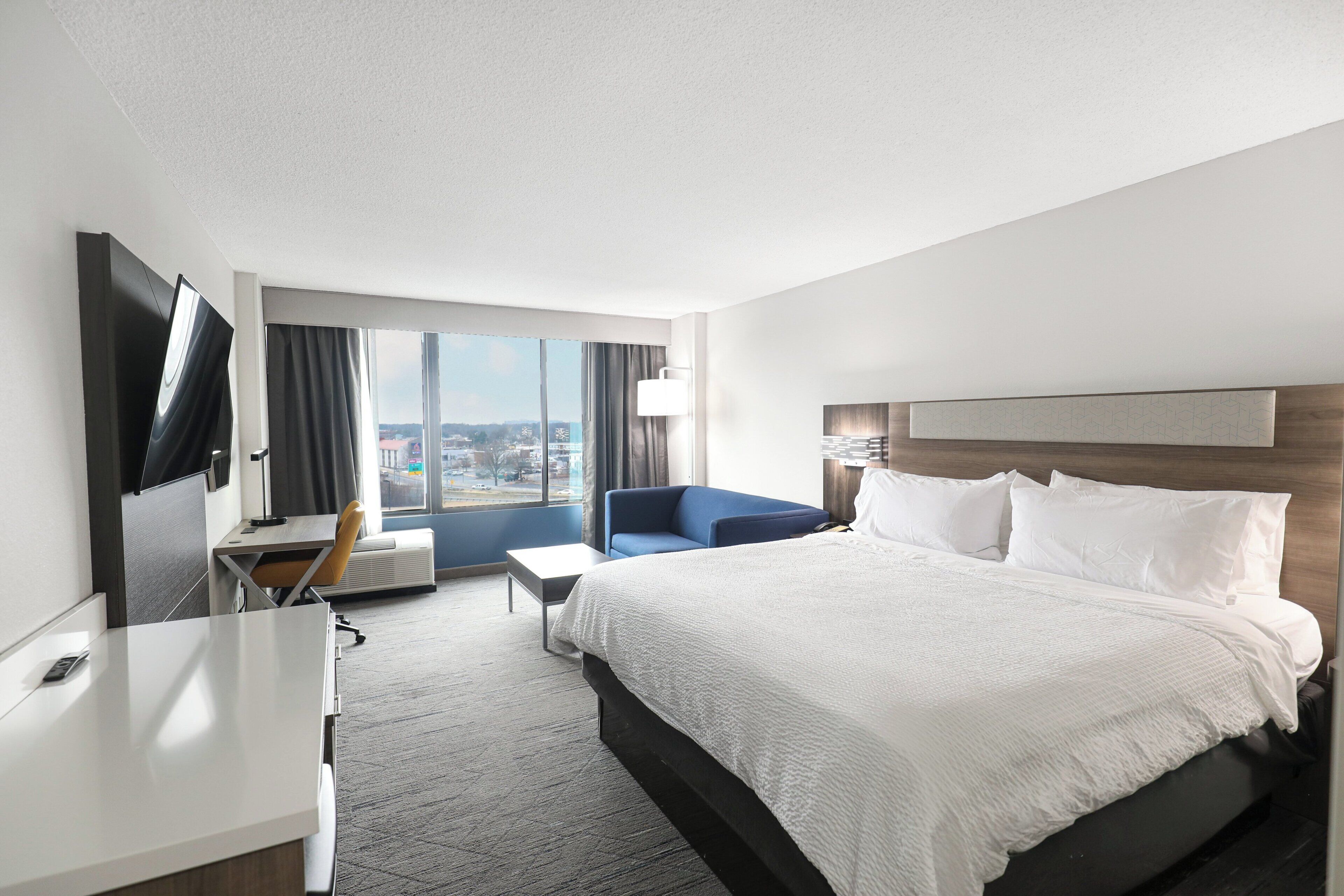 A hotel room with a large bed, a desk, a chair, and a TV.