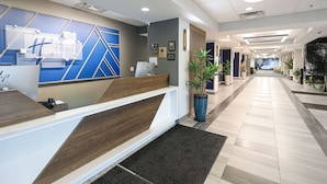 A modern hotel reception area with a blue and white color scheme, a reception desk, and a long hallway with potted plants. - Holiday Inn Express Washington DC SW - Springfield by IHG (Springfield)