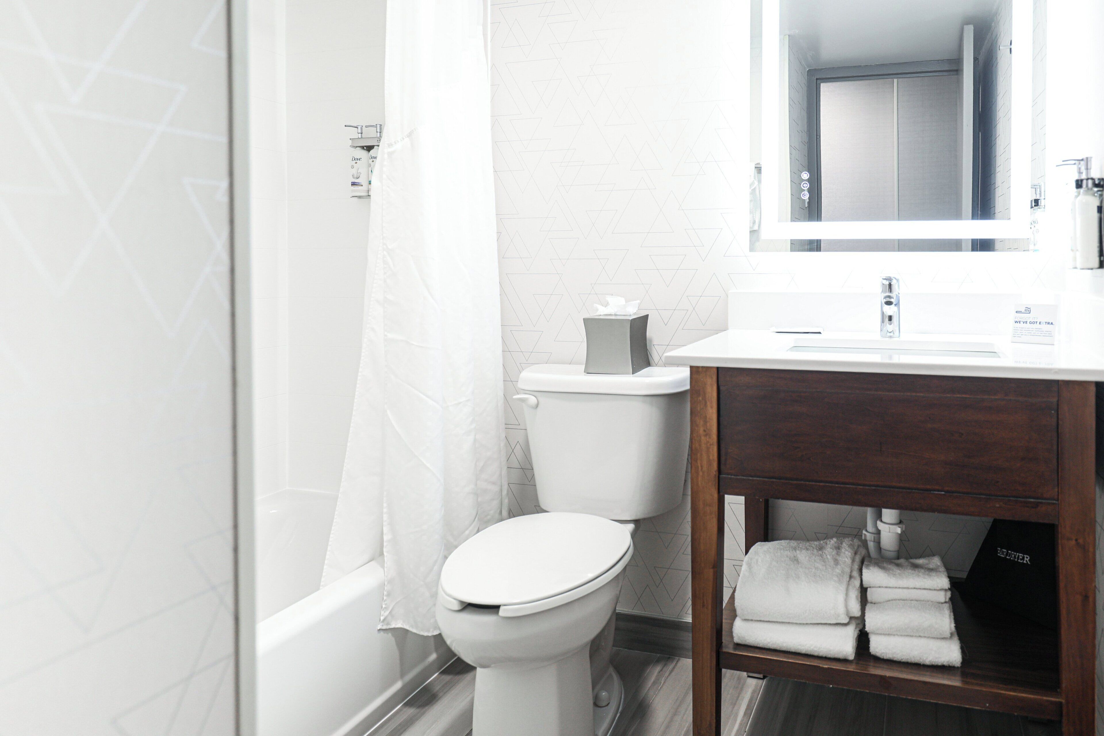 A modern bathroom with a white toilet, a shower curtain, a wooden vanity with a mirror, and a towel rack.