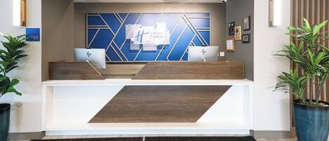 Un comptoir d’accueil au design moderne, avec une palette de couleurs bleu et blanc et des motifs géométriques sur le mur situé derrière.