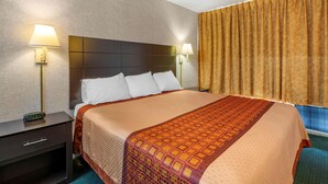 A hotel room with a large bed, two bedside tables with lamps, a nightstand, and a window with curtains. - Rodeway Inn Clearwater - Largo (Clearwater)