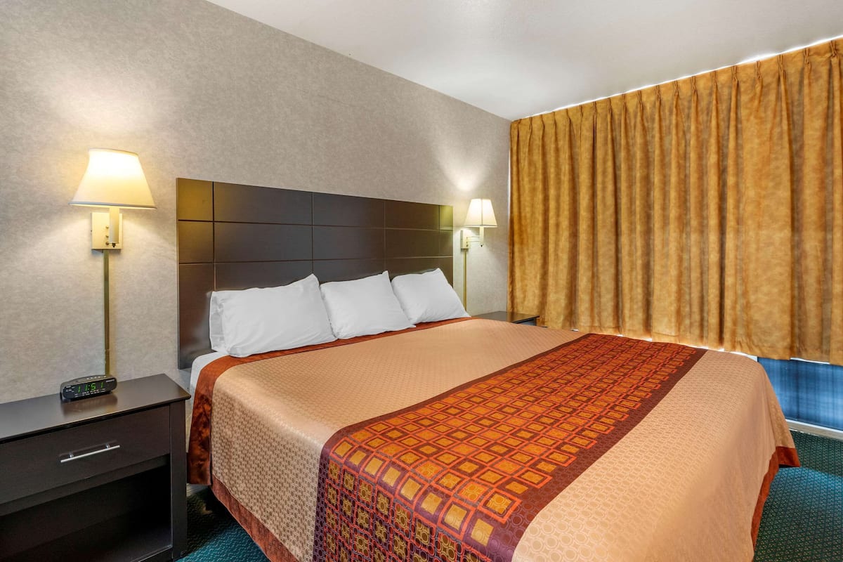 A hotel room with a large bed, two bedside tables with lamps, a nightstand, and a window with curtains.