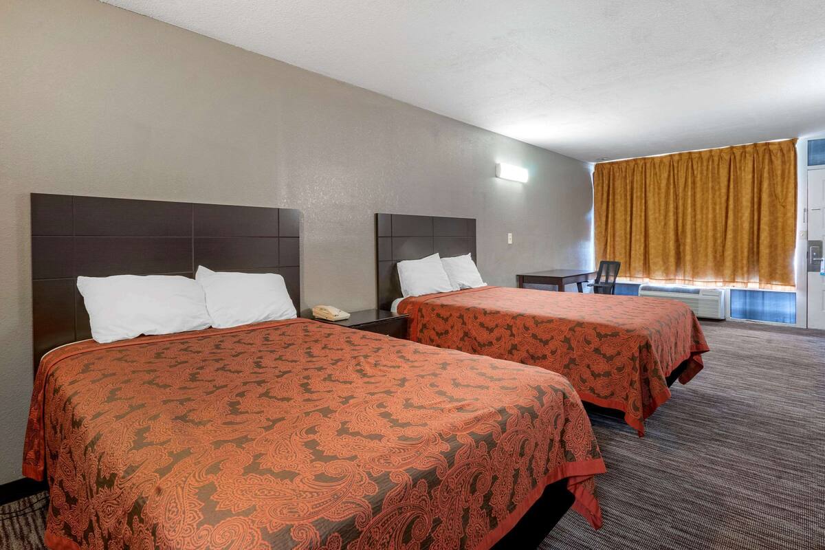 A hotel room with two beds, a desk, and a chair.