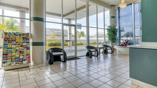 A reception area with a glass door, a magazine rack, two chairs, and a potted plant. - Rodeway Inn Clearwater - Largo (Clearwater)