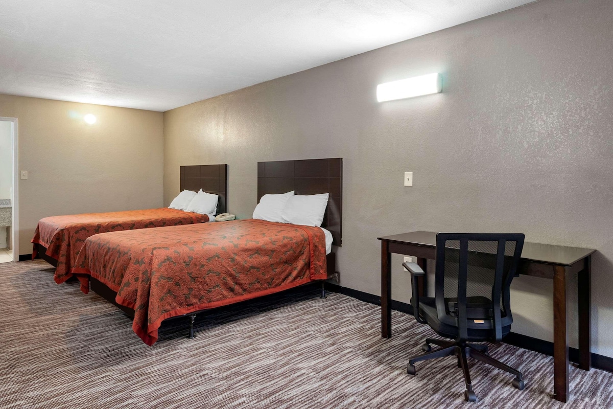 A hotel room with two beds, a desk, and a chair.