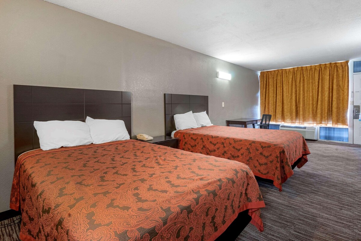Hotellihuone, jossa on kaksi sänkyä, pieni pöytä ja tuoli.