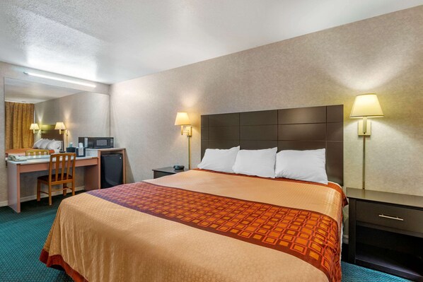 A hotel room with a large bed, a desk with a chair, a microwave, and a nightstand with a lamp. - Rodeway Inn Clearwater - Largo (Clearwater)