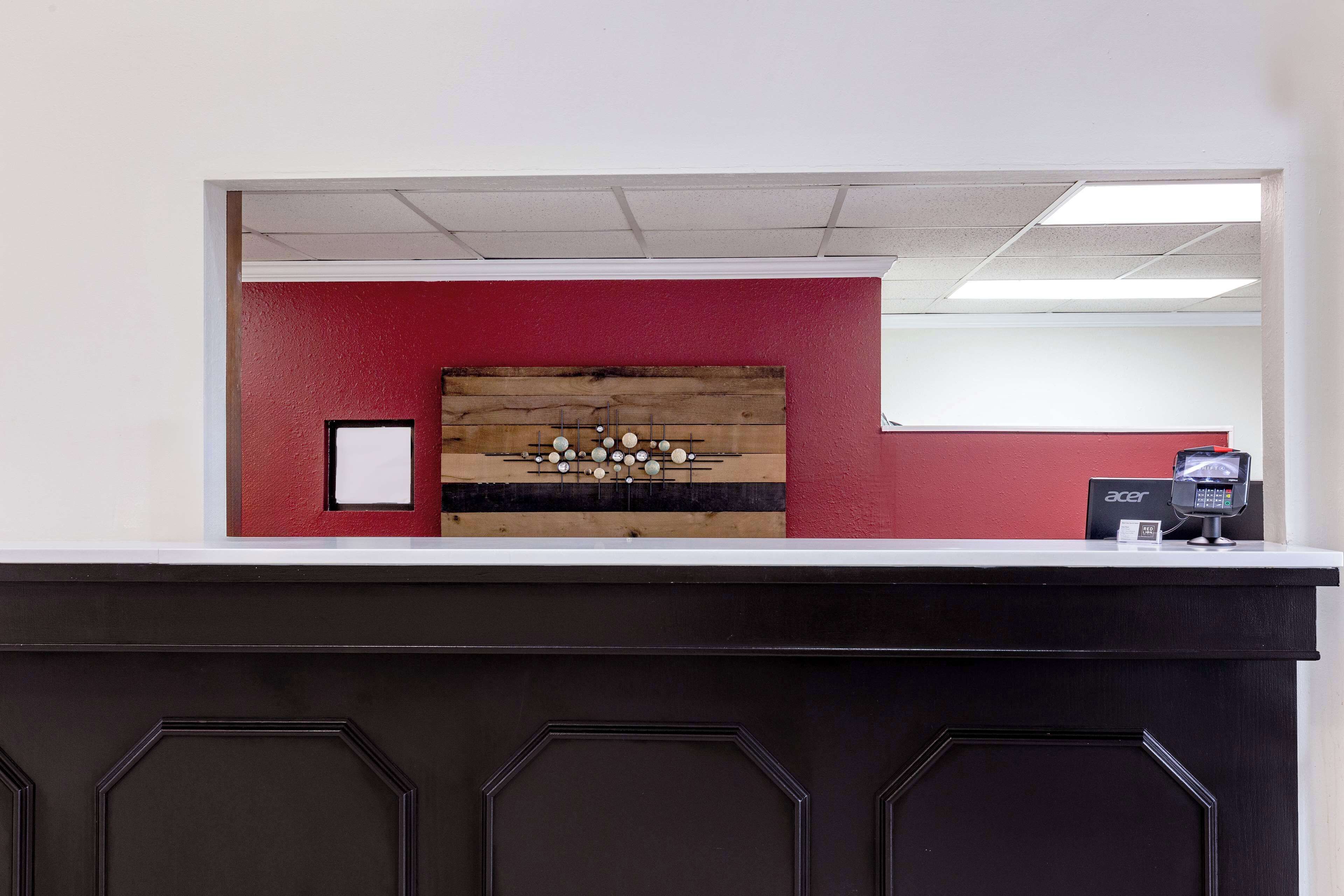 A reception desk with a wooden panel, a red wall, and an Acer monitor.