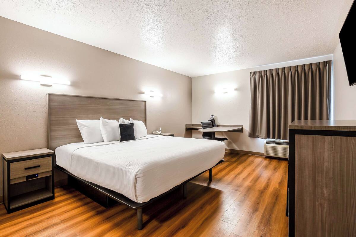 Une chambre d’hôtel avec un lit, des tables de chevet, un bureau et un téléviseur.