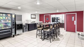 A modern kitchen area with a dining table and chairs, a refrigerator, a coffee machine, and a vending machine. - Red Lion Inn & Suites Pontoon Beach (Granite City)