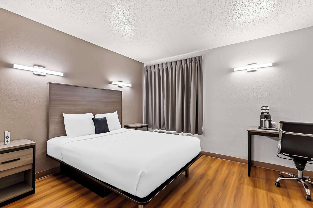 Une chambre d’hôtel comprenant un lit, des tables de chevet, un bureau avec une chaise et une fenêtre avec des rideaux.