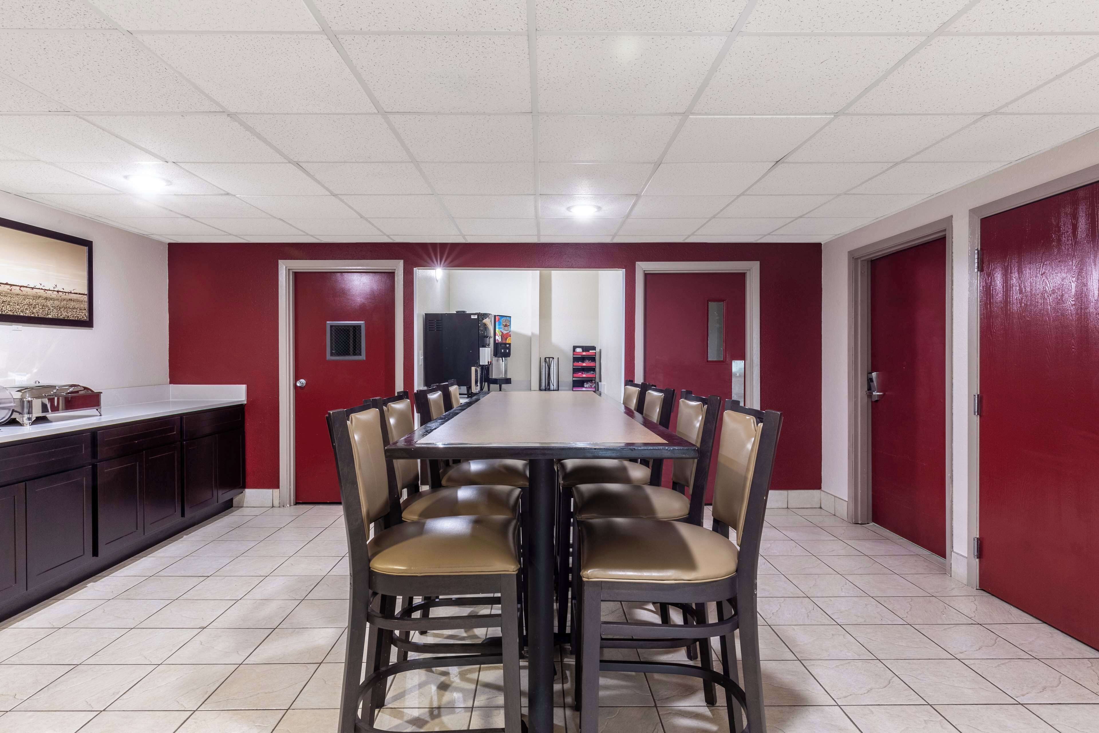 A conference room with a long table and chairs, red walls, and a tiled floor.