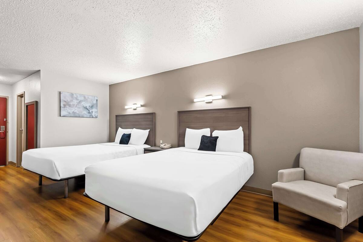 Une chambre d’hôtel avec deux lits, une chaise, un tableau et un téléphone sur la table de chevet.