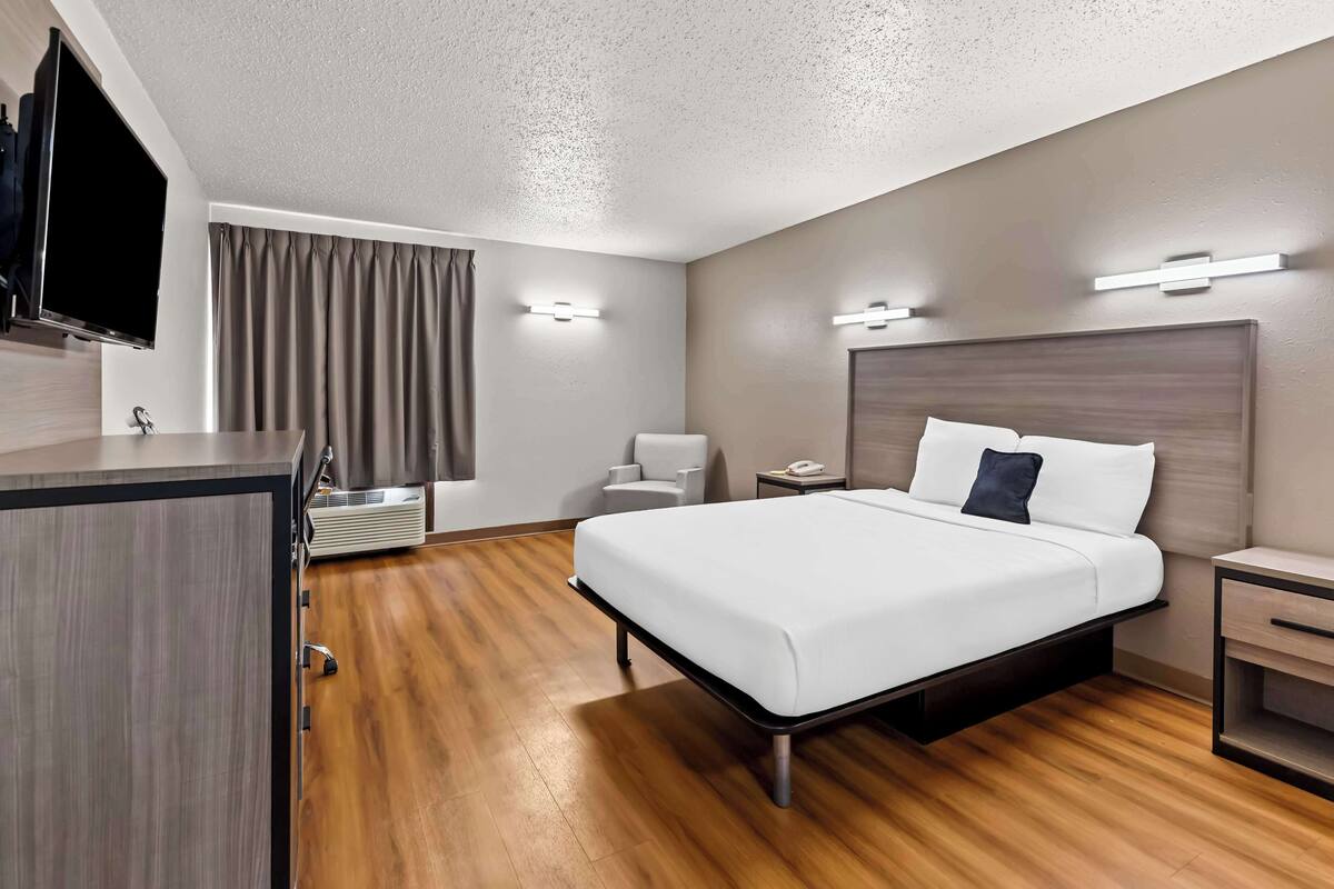 Une chambre d’hôtel moderne dotée d’un grand lit, de tables de chevet, d’un bureau, d’un téléviseur à écran plat et d’une fenêtre avec des rideaux.