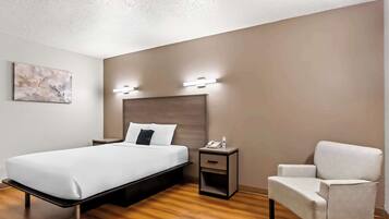 Una habitación de hotel moderna con cama, mesita de noche, silla y lámpara de pared.