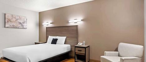Una habitación de hotel moderna con cama, mesita de noche, silla y lámpara de pared.