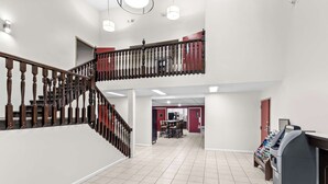 A spacious interior with a high ceiling, a staircase with wooden balusters, and a modern kitchen area in the background. - Red Lion Inn & Suites Pontoon Beach (Granite City)