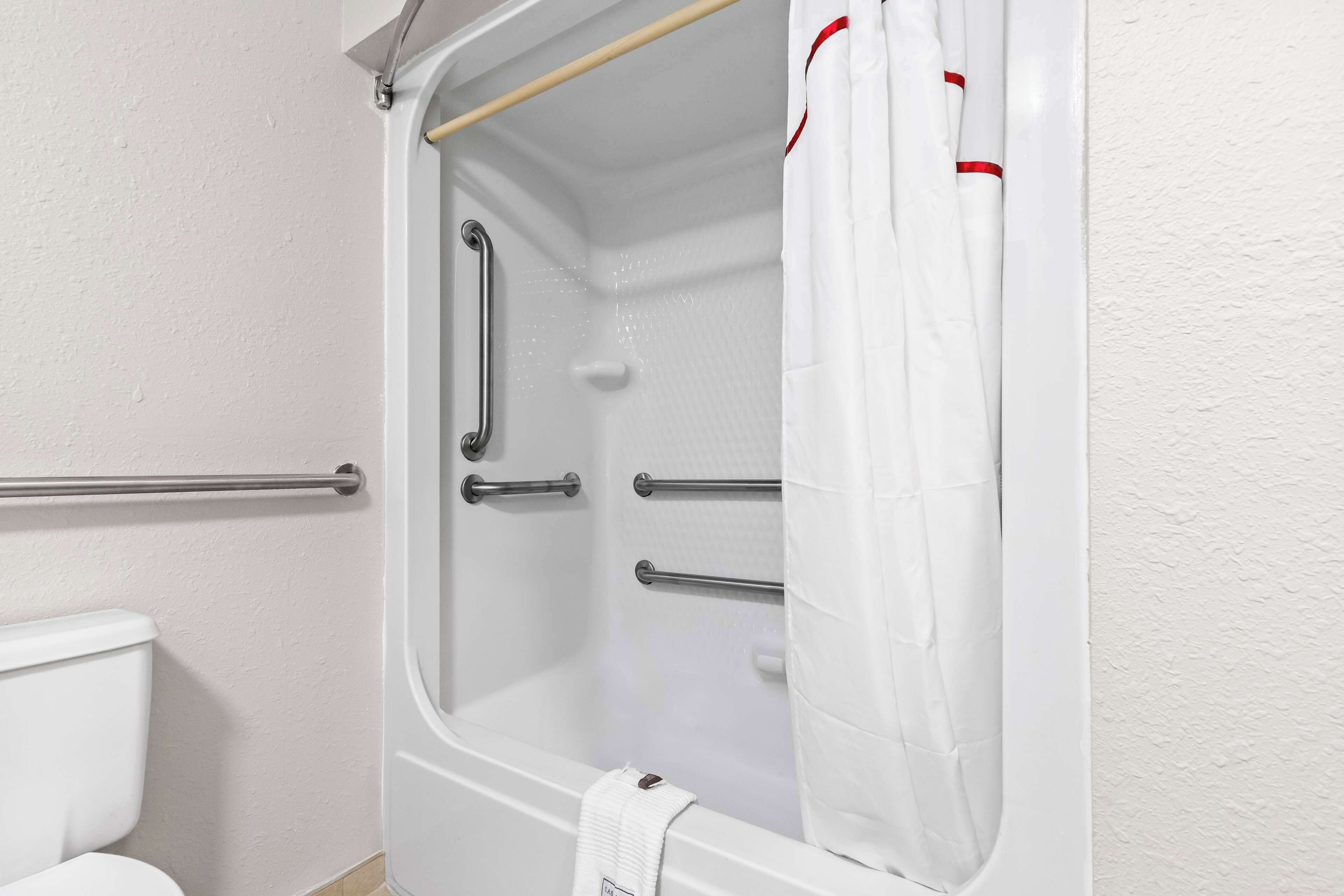 Baño con bañera blanca, barras de apoyo y cortina de ducha.