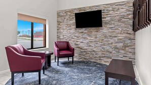 A modern room with a stone wall, a flat-screen TV, two red chairs, a small table, and a view of the outside. - Red Lion Inn & Suites Pontoon Beach (Granite City)