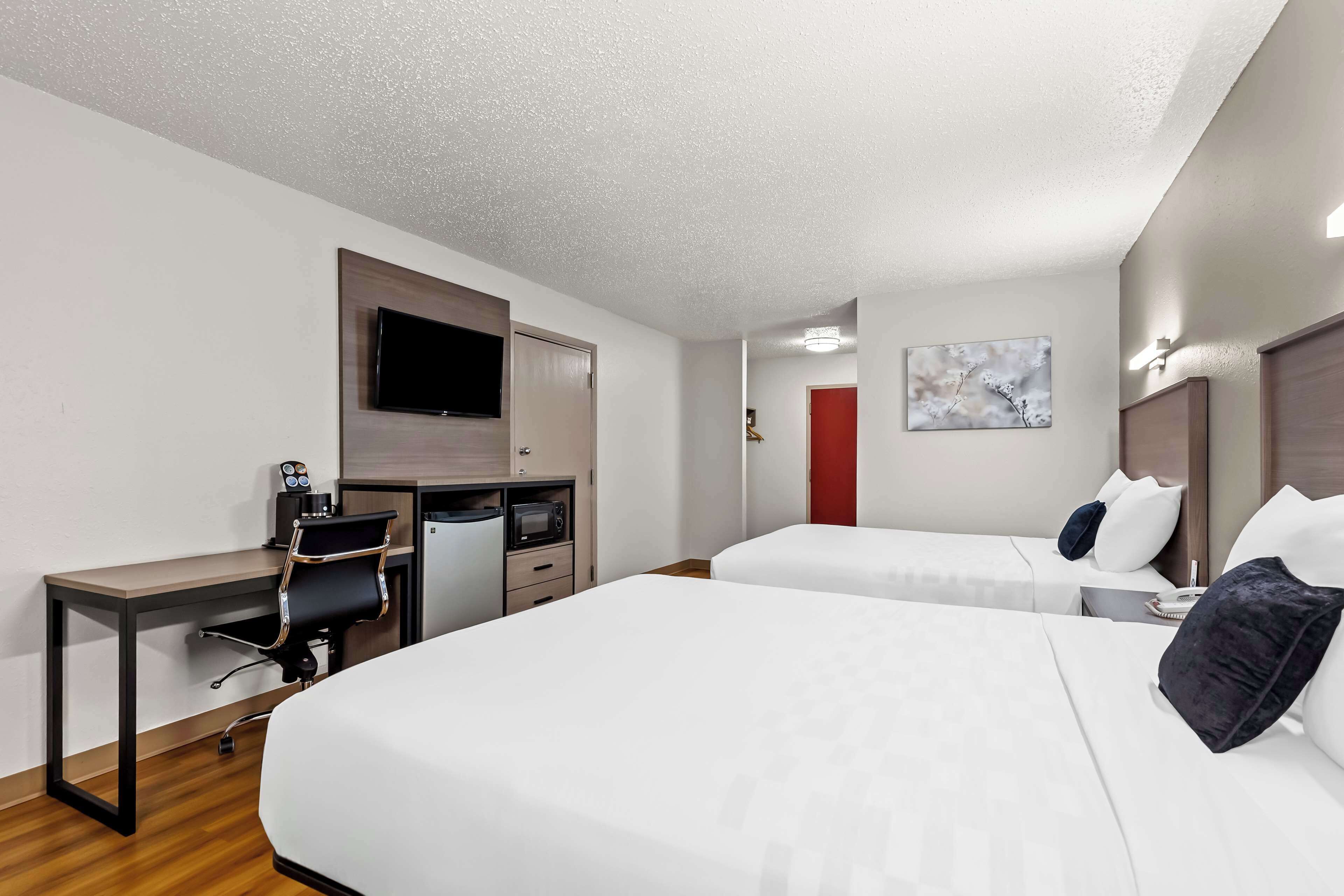 Habitación de hotel con escritorio, dos camas, televisor y puerta roja.