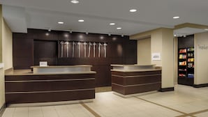 Un espace d’accueil d’hôtel comprenant deux comptoirs de réception, un panneau mural indiquant la marque Marriott Bonvoy, et un distributeur automatique rempli de collations.