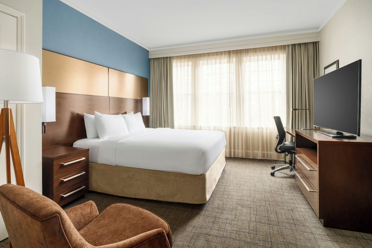 Une chambre d’hôtel avec un grand lit, un bureau avec une télévision, une chaise et une commode.