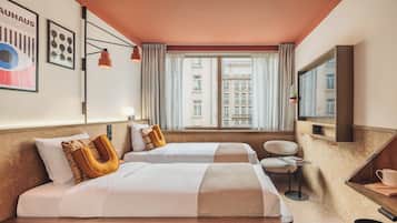 Een hotelkamer met twee bedden, een klein tafeltje, een stoel, een televisie en een raam met uitzicht op gebouwen.