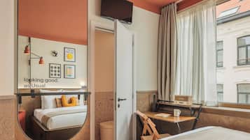 A hotel room with a bed, a desk with a radio, a mirror, and a window with curtains.